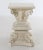 A square two-piece earthenware pedestal in the form of a composite capital with mascarons on a pseudo-Romanesque base with...