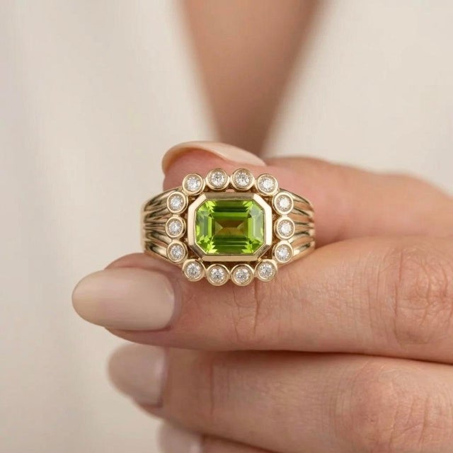 This sophisticated ring features a brilliant emerald-cut center stone framed by a halo of smaller, sparkling stones. Its...