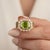 This sophisticated ring features a brilliant emerald-cut center stone framed by a halo of smaller, sparkling stones. Its...