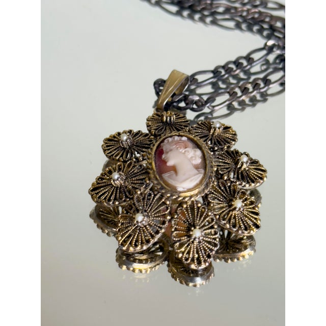 Vintage mid-century cameo pendant necklace featuring a central oval cameo in a filigree-style openwork setting with floral...