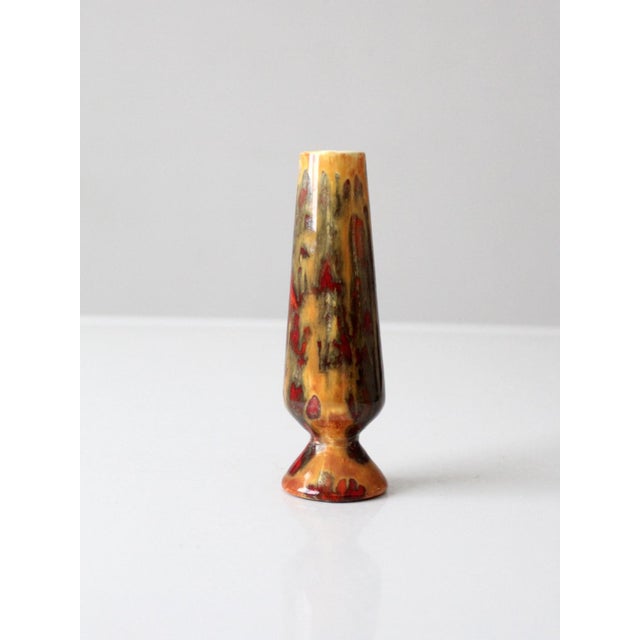 This mid-century studio pottery bud vase features a tall tapered form accented by a richly layered lava glaze in shades of...