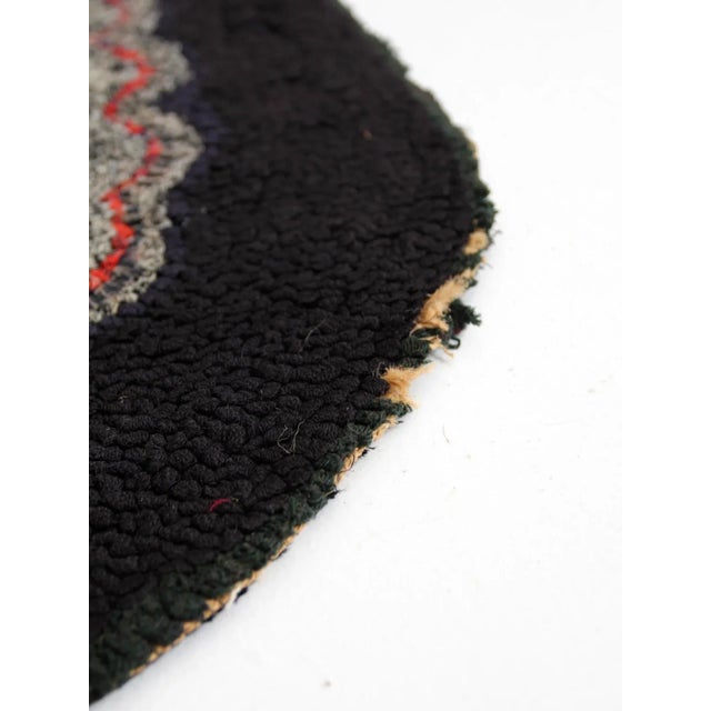 Antique hooked rug in a classic oval shape, featuring a central floral motif against a black background. Handcrafted with...