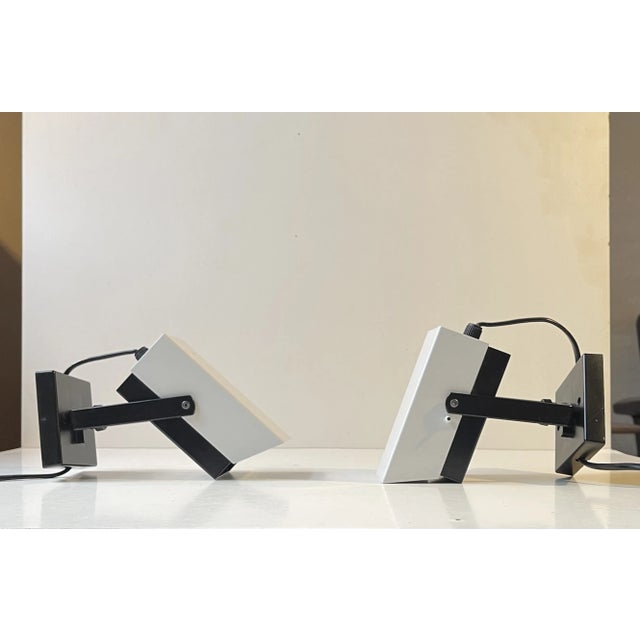 A pair of adjustable wall or night light fashioned in powder-coated steel. A black and a white half featuring strict...