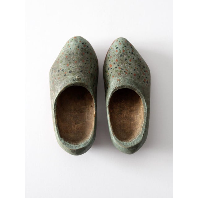 This pair of early 20th century antique wooden clogs features softly worn green paint with hand-applied speckled detailing...