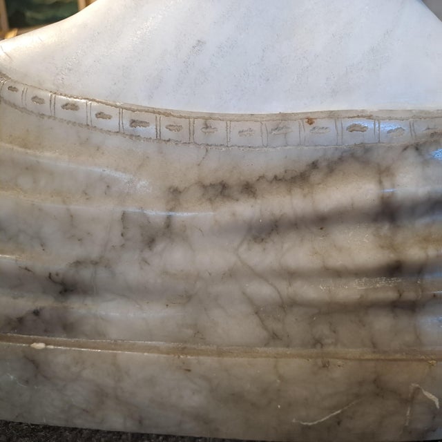 Alabaster sculpture depicting the half-bust of a female figure. The girl, with her face slightly tilted, hints at a smile....