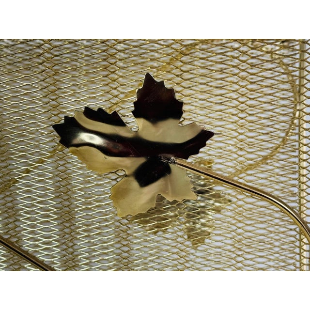 Vintage 1950s gold metal handled magazine rack with a leaf accent. The rack also has a mesh metal design. No marks.