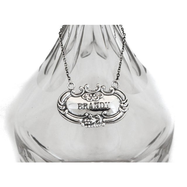 This liquor label is made of sterling silver, with the word "Brandy" engraved on the front in a block font. The perfect...