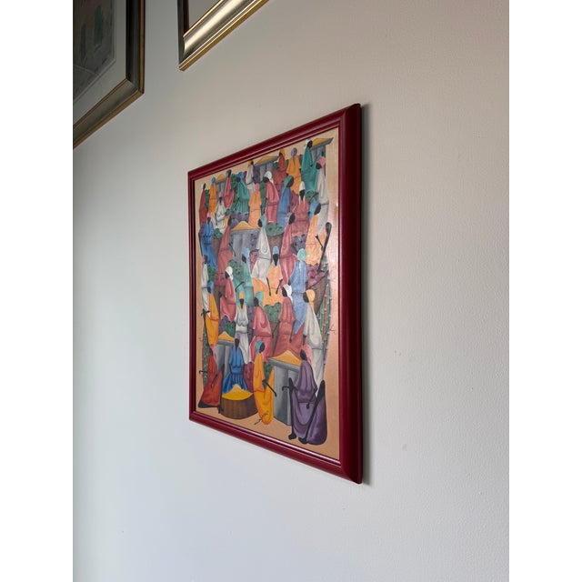 This vibrant vintage Haitian folk art painting depicts a lively market scene rendered in rich, saturated colors and...