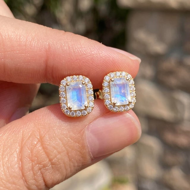 Adorn yourself with captivating iridescence with these delicate halo stud earrings, holding an emerald-cut natural rainbow...