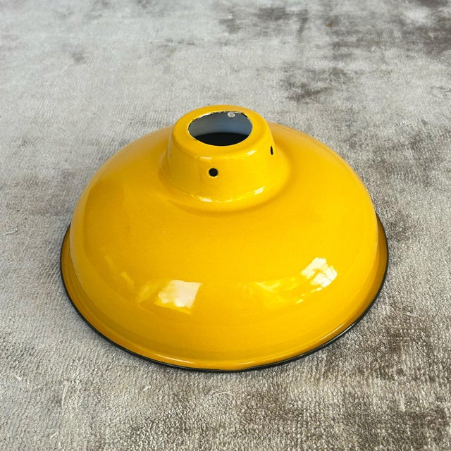 Mustard yellow enamelled coolie shade with glossy exterior, black rim, and white inner reflector. The wide dome form...