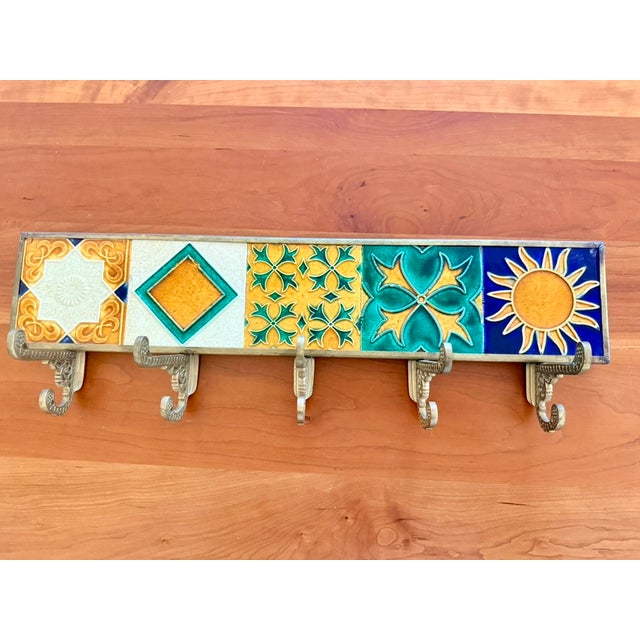 A striking vintage brass wall rack featuring five raised ceramic art tiles inspired by the bold geometry and stylized...