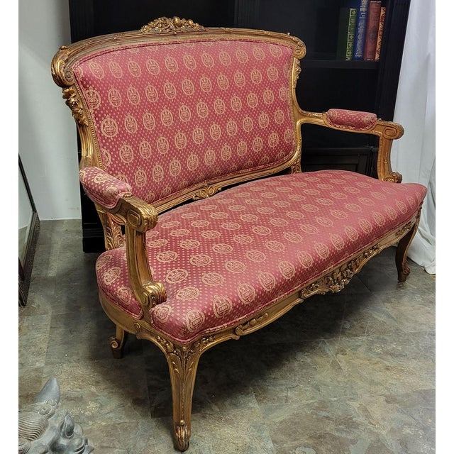 A beautifully carved French Louis XV-style giltwood settee featuring a graceful serpentine silhouette, floral and foliate...