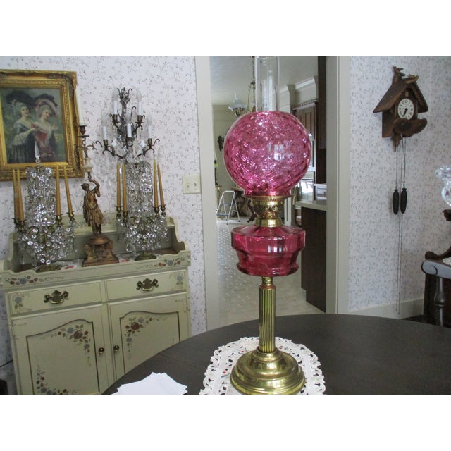 This antique brass column tall oil lamp features a Victorian style with a double burner and a cranberry glass shade,...