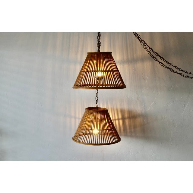 Vintage pair of handwoven bamboo and rattan pendant lamps featuring a tapered conical shade design with vertical slats....