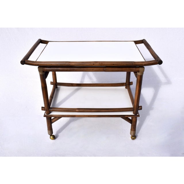 1960s Pagoda style bamboo two tier white laminate bar cart on brass casters in the manner of John Wisner for Ficks Reed. A...