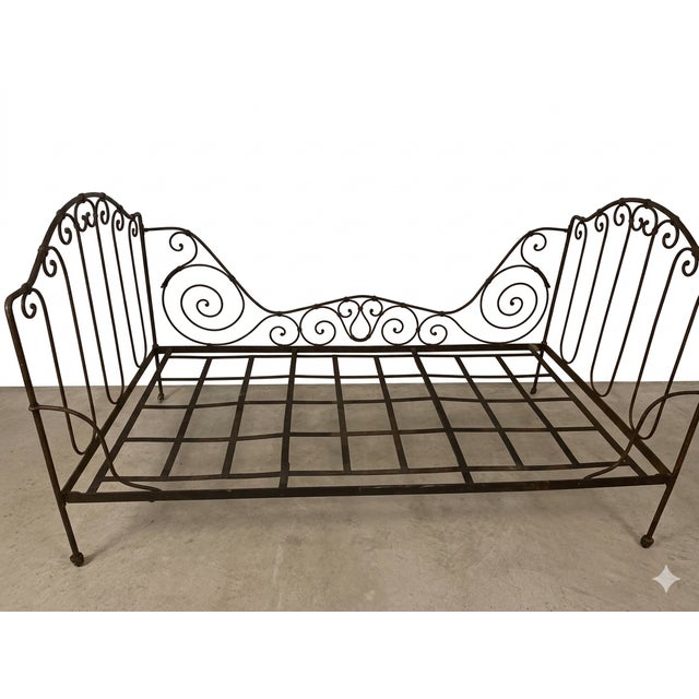 An exceptional, authentic 19th-century French wrought iron campaign daybed featuring striking, intricate scrollwork on the...