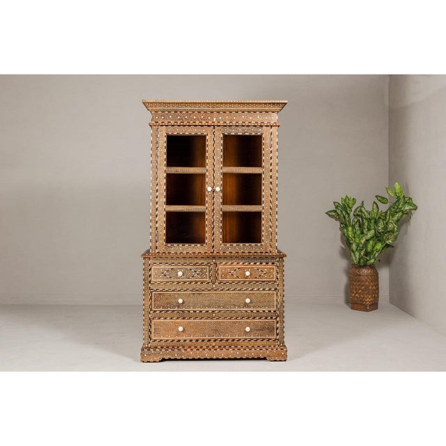 An Anglo-Indian style two part buffet à deux-corps with glass doors, abundant bone inlaid floral-themed décor, and four...