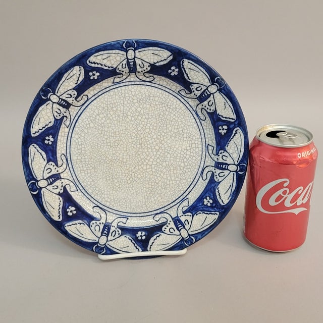 A hand-painted Dedham Pottery plate decorated with a repeating moth motif in rich cobalt blue against a crackled ivory...