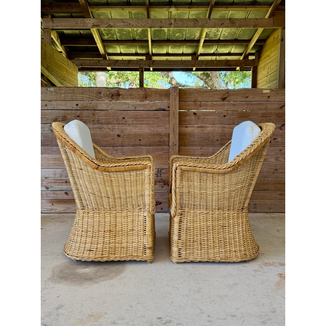 A beautiful pair of vintage woven rattan and wicker lounge armchairs featuring sculptural curved backs, gracefully sloping...