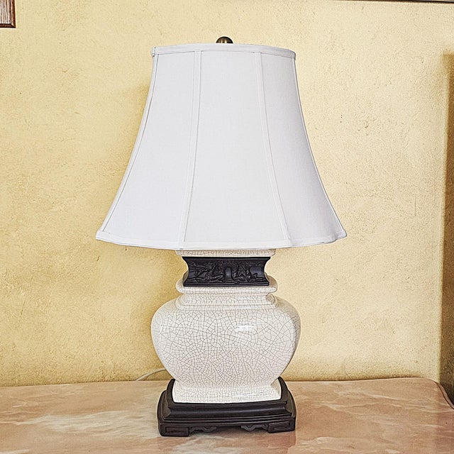 Elegant vintage ceramic lamp featuring a white crackle‑glaze body, dark carved mid‑band, and a white tapered fabric shade....