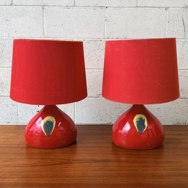 A pair of ceramic table lamps by Bjørn Wiinblad for Rosenthal, finished in a deep red glaze with blue and yellow...