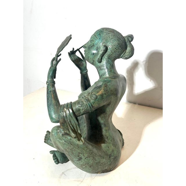 Elegant patinated bronze sculpture depicting a seated female figure holding a small hand mirror. The pose is serene and...