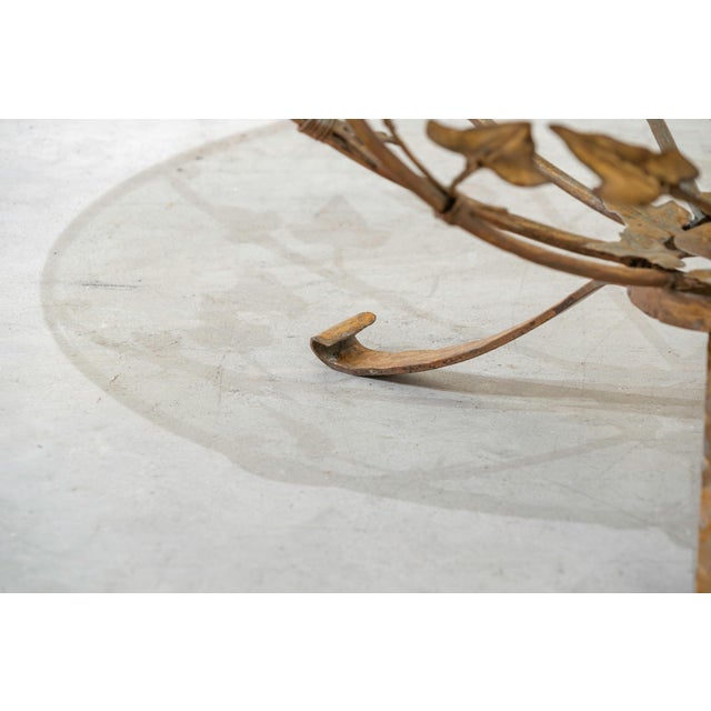 Circular side table in wrought iron, gilded with a design of vine leaves and foliage, with a glass top. The table is...