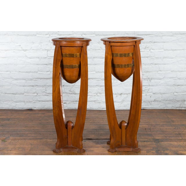 A pair of Javanese Art Deco style teak wood plant stands from the 20th century, with tall proportions, horizontal brass...