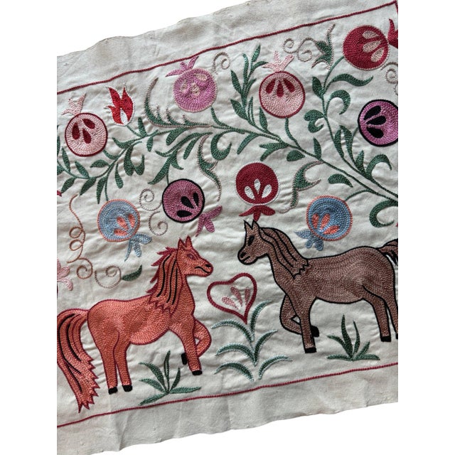 Hand-embroidered Suzani panel from Uzbekistan, worked in fine floss on a cream cotton ground. Two horses and a donkey move...