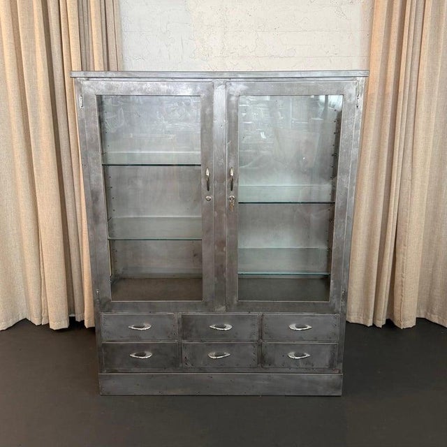 This industrial, double-wide, brushed steel, medical apothecary display cabinet is circa the early 1940s. The cabinet...