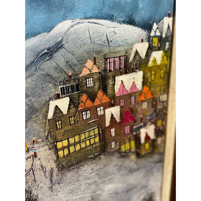 This artwork is a mixed-media/3D collage painting depicting a whimsical winter village built into a snowy, mountainous...