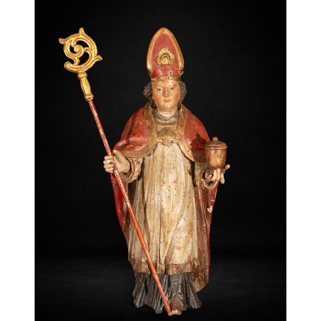 A finely carved and polychromed wooden sculpture depicting a bishop saint, traditionally identified as Saint Rupert,...