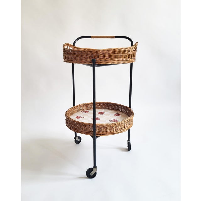 A charming Austrian bar trolley from the 1950s, its black lacquered iron frame carrying two oval woven rattan baskets, the...