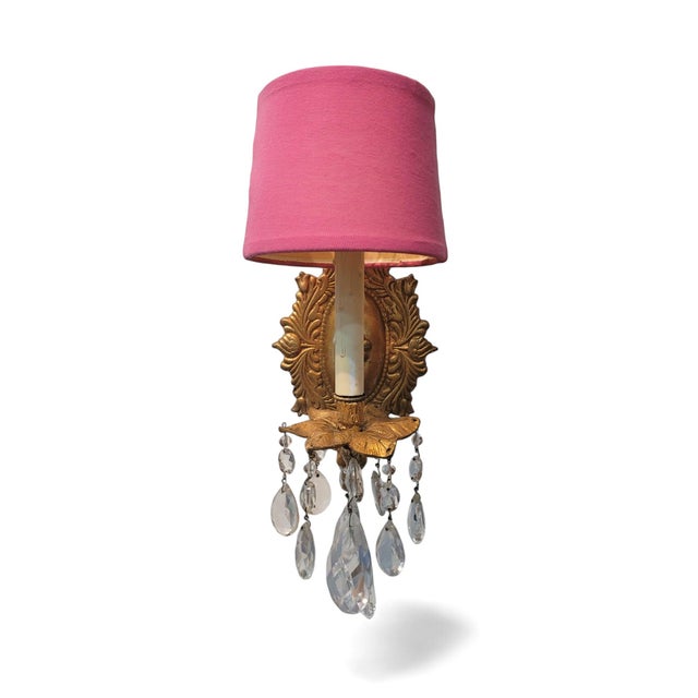 A pair of elegant, electrified wall sconces featuring vibrant pink shades and ornate gilded metal backplates in a floral...