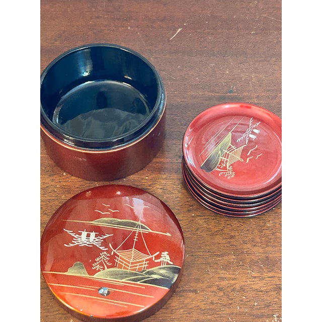 A striking mid-20th-century Japanese lacquerware coaster set featuring six individually decorated coasters housed in their...