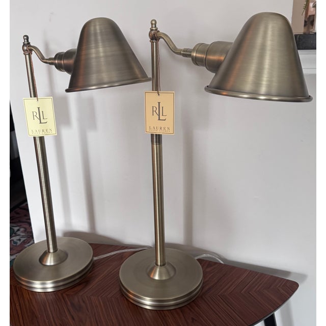A sophisticated pair of authentic Ralph Lauren swing arm table lamps crafted in a brushed brass finish with classic metal...