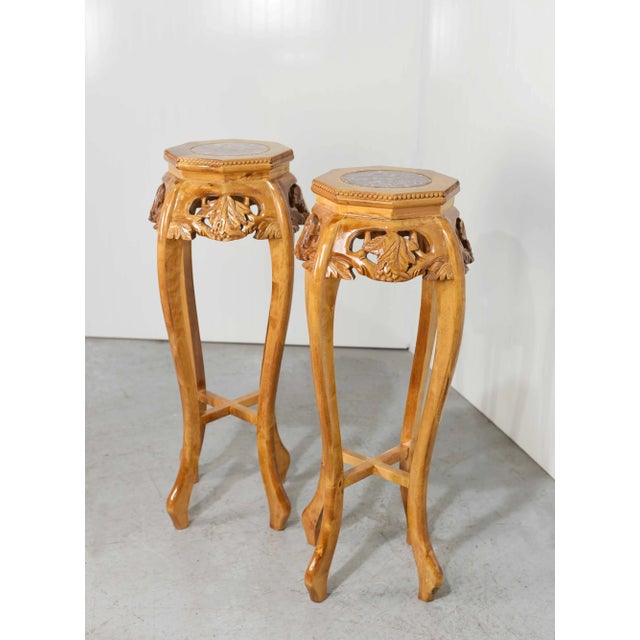 This pair of Mid Century Chinoiserie Carved Wood Marble Top Plant Stand Pedestal Tables features a pink and brown marble...