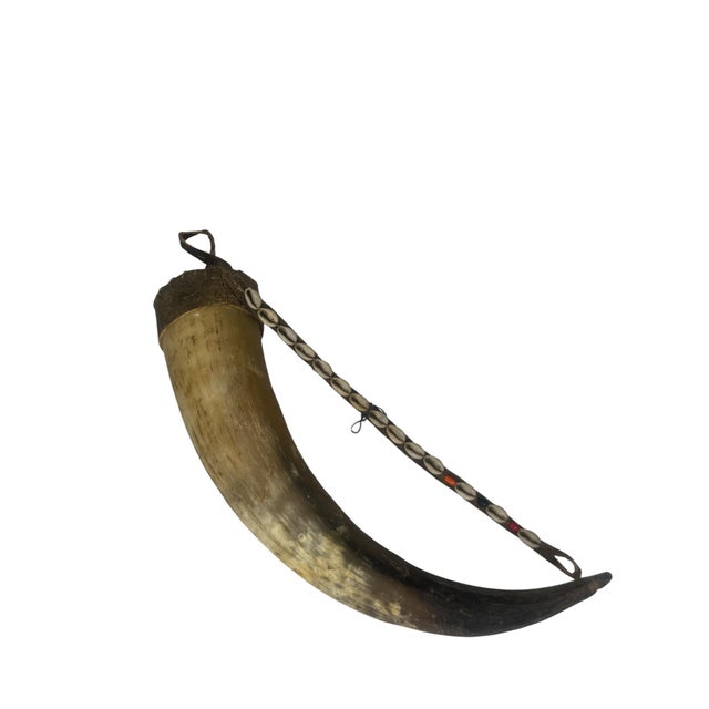 A substantial African ceremonial horn with hand-stitched hide and fur cap, a full line of cowrie shells running the length...