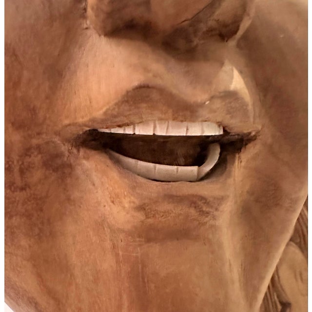 A carved wood figural head mounted on a black display stand, depicting a serene female face with a gentle, slightly parted...