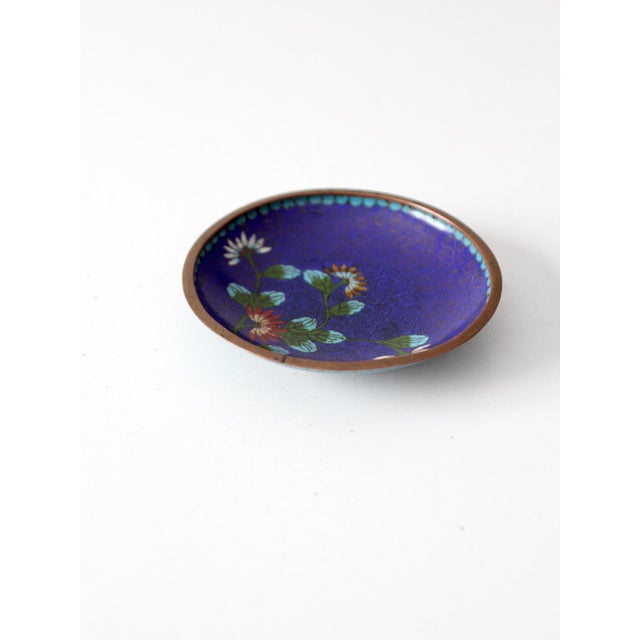 Vintage Chinese cloisonné dish featuring colorful florals against a rich cobalt blue ground, accented by delicate...
