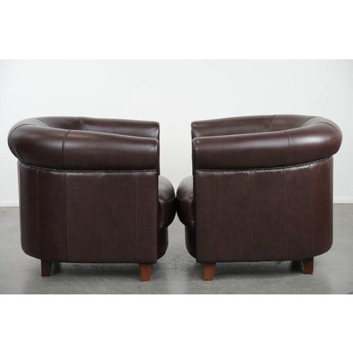 Offered in very good condition, this set of two English-style cowhide club chairs in a unique brown/dark purple color...