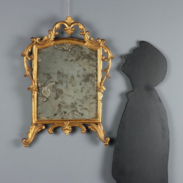 Carved and gilded wood mirror, featuring a molded frame that highlights elegant foliate carvings and scrolls. The mercury...