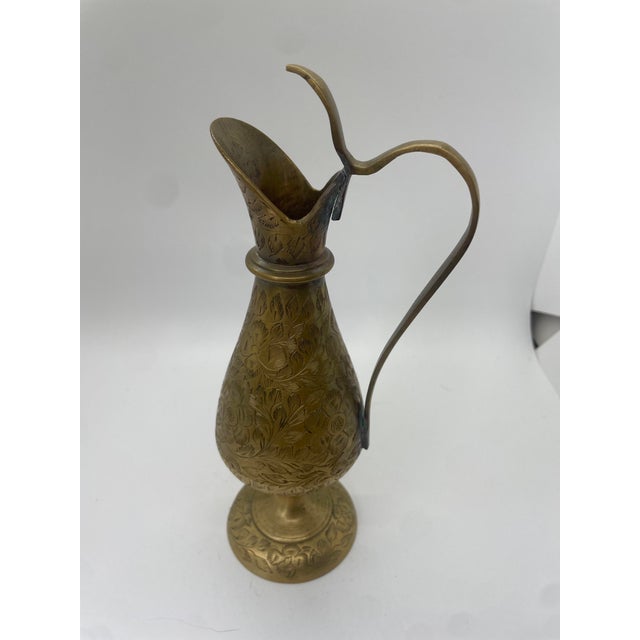 A charming brass pitcher adorned with intricate flower details and a gracefully curved handle. This elegant piece exudes...