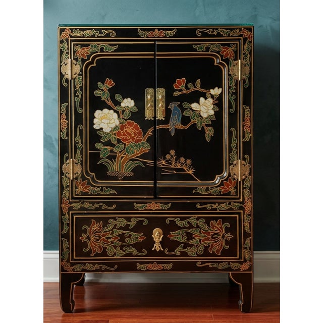 A charming vintage Chinoiserie accent cabinet featuring a glossy black lacquer finish with colorful floral, foliage, and...