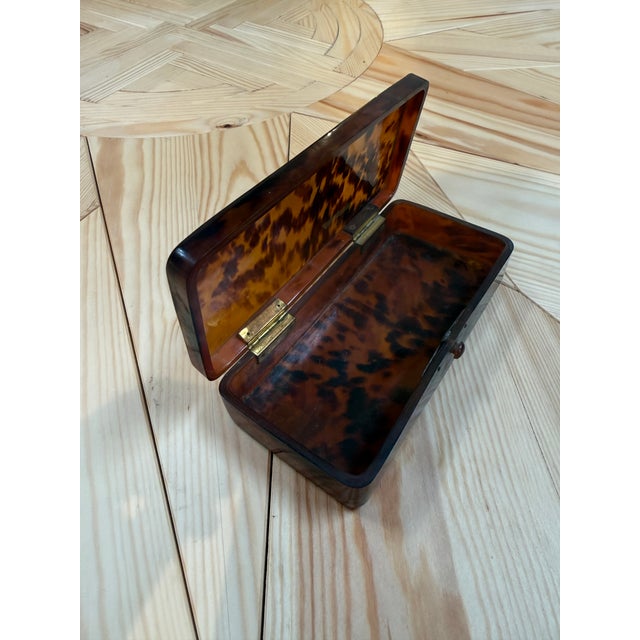 A long, rectangular box crafted from lucite finished in a rich faux-tortoiseshell pattern, with mottled tones of amber,...