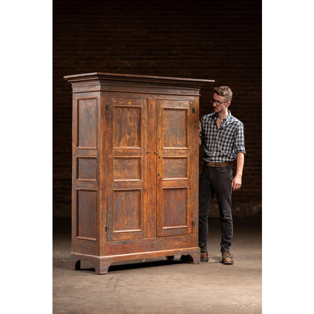 Tall two-door cupboard constructed of solid pine with a deeply worn painted surface and original hardware throughout. The...