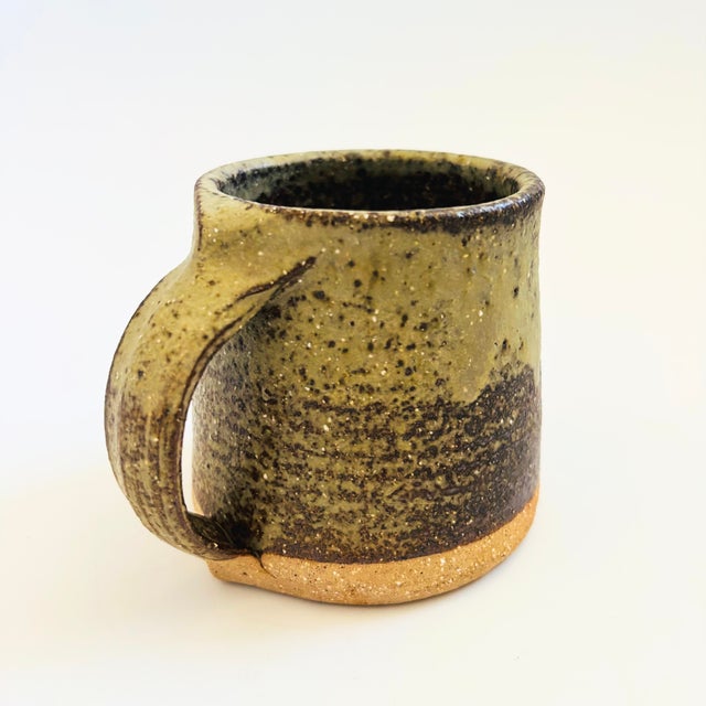 A vintage studio pottery mug. Two toned earthy colored glazes with a contrasting unfinished base. Marked on the bottom by...