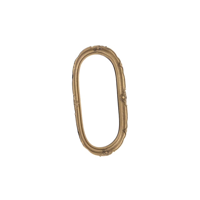 An elegant, oval mirror in a gilded frame, originating from Poland in the 1950s. The frame features a richly decorated,...