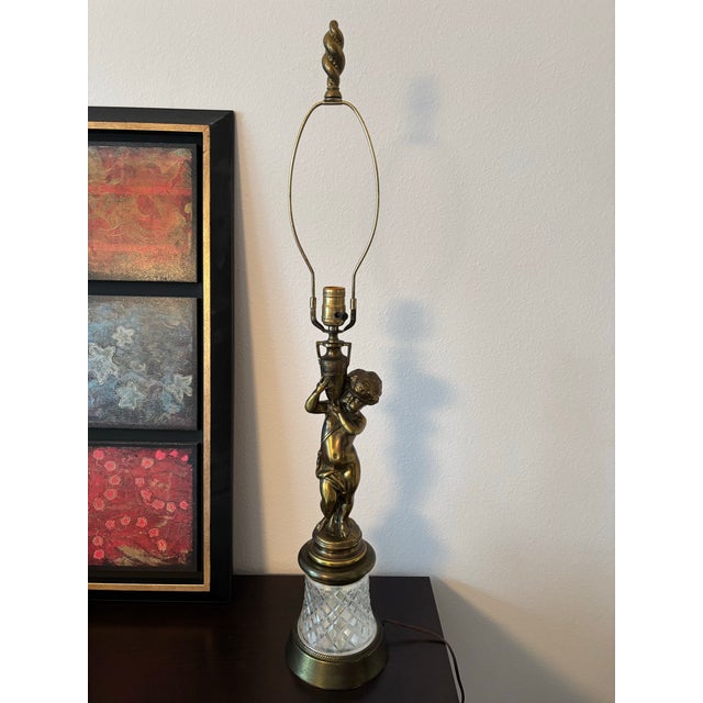 A beautifully detailed mid‑century brass lamp featuring a sculpted cherub standing atop a faceted cut‑glass base with a...