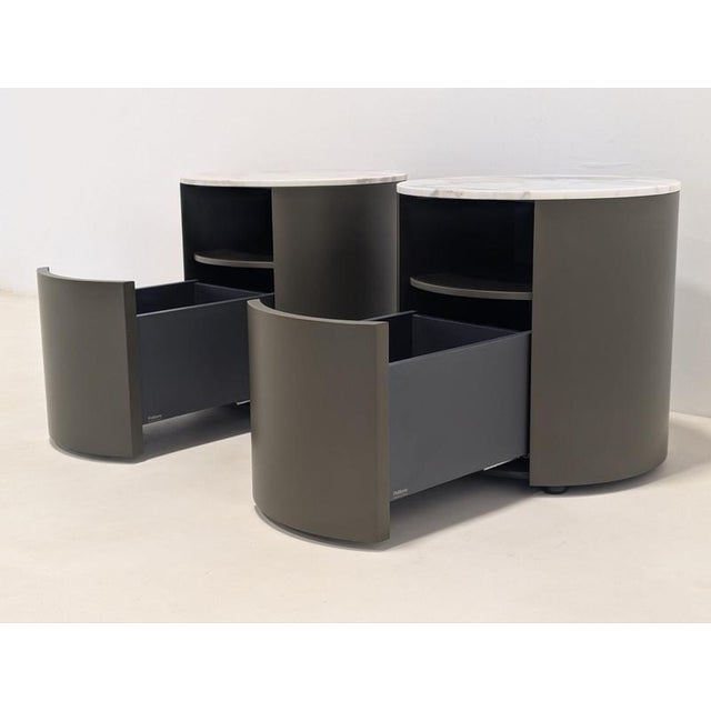 The Poliform Onda nightstands feature a sleek, cylindrical design with a smooth taupe finish, an open upper shelf, and a...
